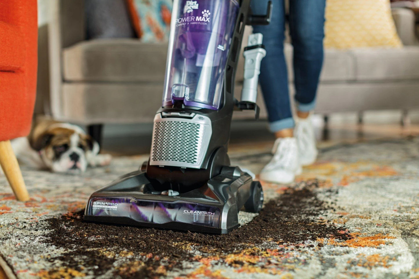 A purple and grey pet vacuum cleans up spilled soil from a plant off of a carpet