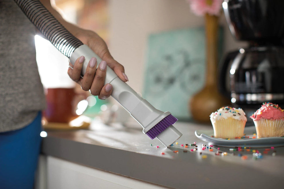 A purple and silver attachment tool vacuums up spilled sprinkles from cupcakes